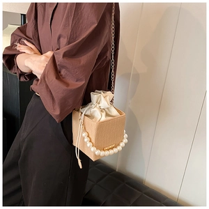 Detail of apricot box bag featuring vertical wavy texture, pearl handle, and gold chain strap