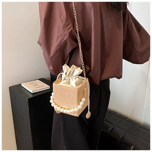 Close-up of beige pleated bucket bag with pearl handle and golden chain shoulder strap