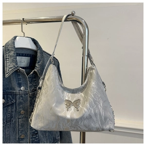 Detail of silver pleated hobo bag featuring metal butterfly ornament and slender strap