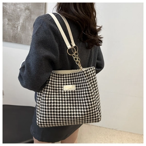 Close-up of houndstooth tote bag detail featuring gold chain strap and leather patch