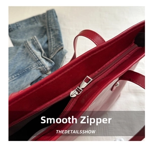 Detail of a smooth silver zipper closure on a large red faux leather tote bag
