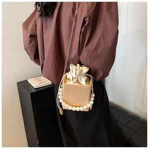 Detail view of straw bucket bag with pearl handle and metal chain on a black stand