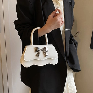 Petit sac à main blanc avec nœud en métal argenté et rabat ondulé sur fond de costume noir