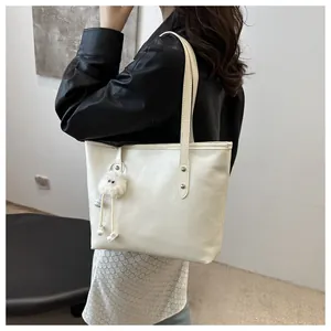 Close-up of a white leather tote bag with a plush charm and fashion typography on the side