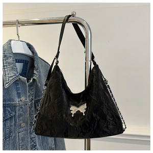 Detail of black wrinkled underarm bag with silver bow and leather strap on metal rack
