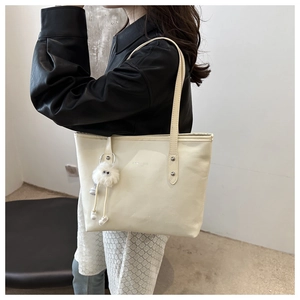 Off-white tote bag detail with long shoulder strap and fuzzy monster charm accessory