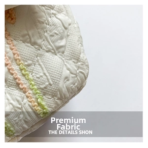Detail of white quilted fabric with pink and green woven rope textures on a handbag