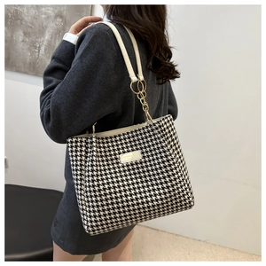 Detail of houndstooth tote bag showing leather handles and gold metal chain hardware