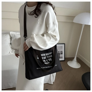 Detail of black canvas tote bag showing wide brown handle and white letter printing