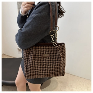 Detail of houndstooth tote bag featuring a leather logo and gold chain strap accents