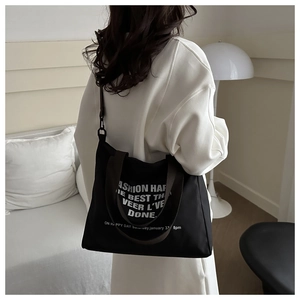 Detail of black canvas tote bag with brown handles and white artistic lettering