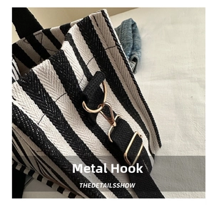 Detail showing the golden metal hook and woven strap of the striped canvas bag