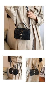 Detail view of black leather crossbody bag featuring gold horseshoe buckle and long strap