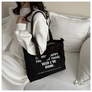 Detail of a large black canvas tote bag with white typography and brown straps