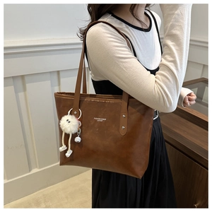 Brown leather tote bag with plush charm and shoulder strap shown on a model