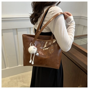 Brown faux leather tote bag with plush charm shown from side view on model