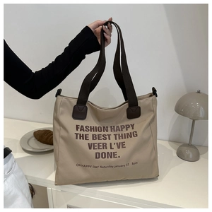 Detail of canvas tote bag with brown straps and slogan print held by a model