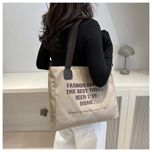 Detail of minimalist beige canvas tote bag with contrast brown straps and slogan print