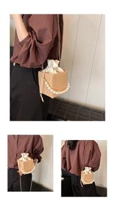 Detail of woven bucket bag featuring pearl handle, gold chain and drawstring liner