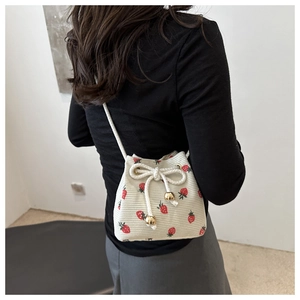 Detail of a beige corduroy bucket bag with red strawberry prints and drawstring design