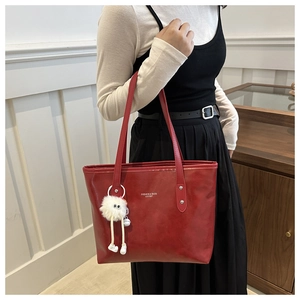 Red leather tote bag with white logo and a cute plush monster charm accessory