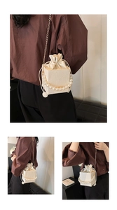 Detail of cream drawstring bucket bag featuring a large pearl handle and gold chain strap