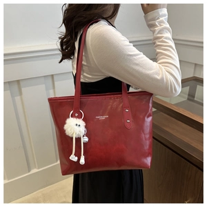 Detail of red large capacity tote bag with white text and plush charm on the shoulder