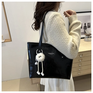 Detail of glossy black leather tote bag featuring white text and a plush monster charm