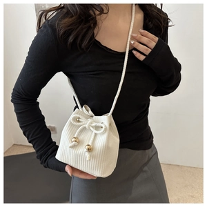 Detailed view of a white woven bucket bag featuring gold beads and thin rope strap details