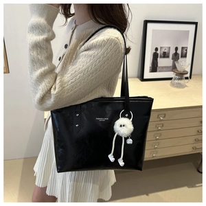Detail of black leather tote bag with white plush doll charm and fashion lettering text