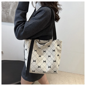 Gros plan d'un sac fourre-tout en velours beige avec motif losanges et petits nœuds noirs