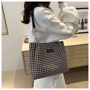 Detail of houndstooth tote bag with elegant gold chain strap and brand logo plate