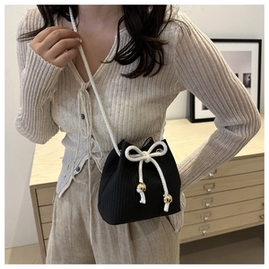 Detail of black drawstring bucket bag with vertical texture and large white rope bow