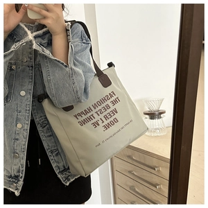 Mirror selfie showing a large canvas tote bag with brown artistic lettering and shoulder strap