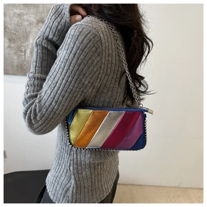 Detail of vibrant metallic leather crossbody bag with silver studs on grey knitwear