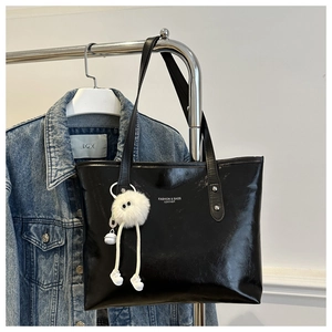 Detail of black glossy leather tote bag with white plush charm on denim background