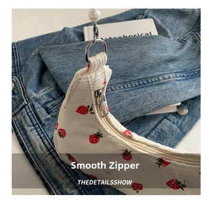 Detail of smooth metal zipper and strawberry print on beige corduroy underarm bag