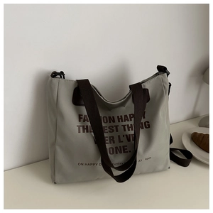 Detail of grey-green canvas tote bag with brown straps and artistic text on desk
