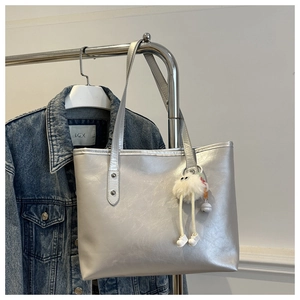 Silver metallic tote bag with plush monster charm accessory and thin shoulder straps