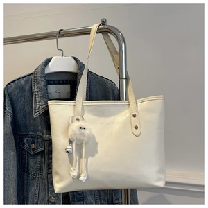Detail of off-white tote bag with gold lettering and cute plush monster charm accessory
