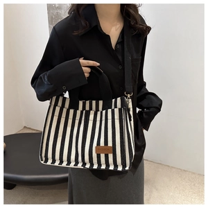 Detailed view of the striped canvas tote bag with a brown leather logo patch and black handles