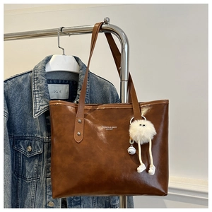Brown vintage faux leather tote bag detail with white cartoon pompom charm and logo text