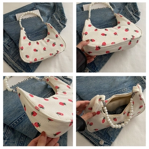 Detail of white corduroy dumpling bag with strawberry print and pearl bead handle