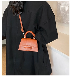 Crossbody orange leather bag with pebbled texture and metal buckle on back of model