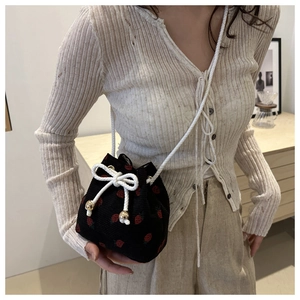 Detail of strawberry print corduroy bucket bag with drawstring and gold metal bead accents