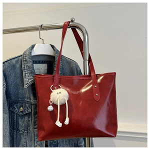 Detail of red leather tote bag featuring a cute plush pendant and shoulder strap