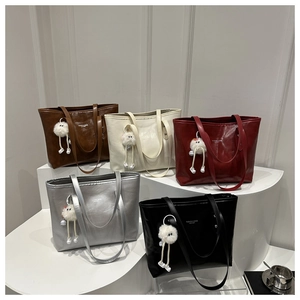 Five colored tote bags with fuzzy charms displayed on a minimalist white platform