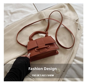 Detail of orange-brown pebble leather mini bag with horizontal buckle on beige jacket