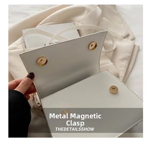 Close-up of golden magnetic buckle and neat stitching on white leather handbag