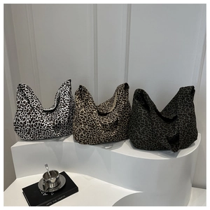 Three leopard print canvas tote bags in black, brown and grey displayed on a podium